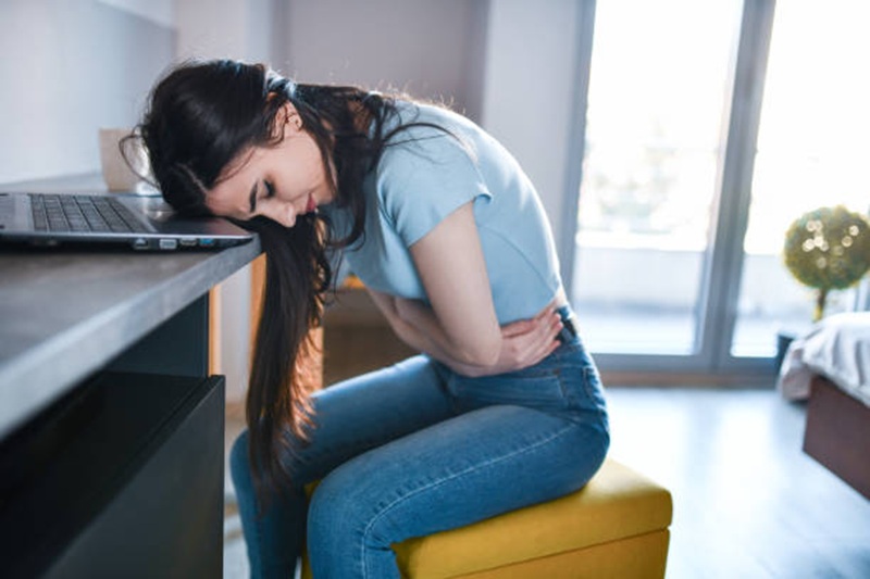 Female With Stomach Pain Curling Up After Working Too Much On Laptop